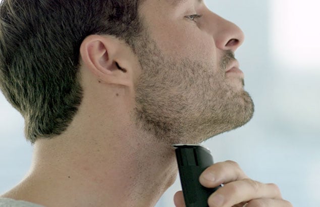 Ein Mann rasiert seine Bartlinie am Hals mit einem elektrischen Barttrimmer von Philips.