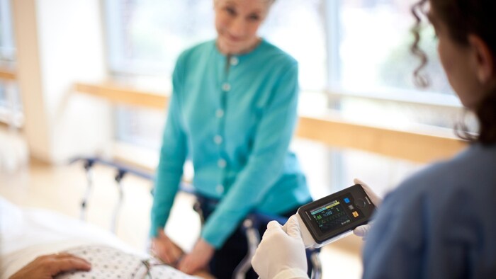 Eine Person hält einem Patienten ein Gerät hin