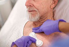 Ein Sensor wird auf der Brust eines älteren Patienten in einem Krankenhausbett platziert.