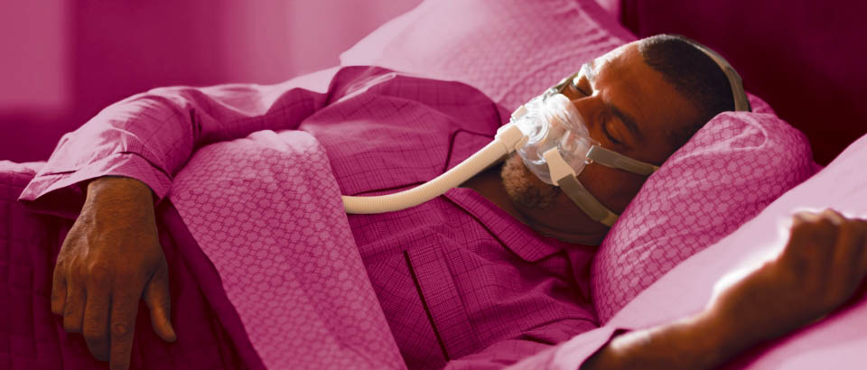 Mann in pinkfarbenem Outfit, der mit einer Maske schl&auml;ft