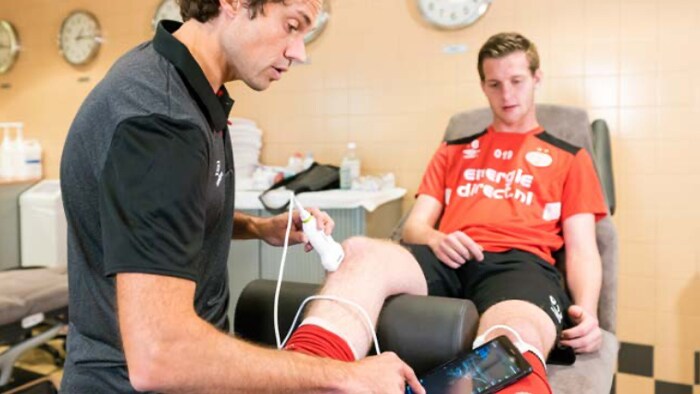 Medizinische Fachkraft beim Einsatz des Handheld-Ultraschallgeräts am Knie eines Sportlers