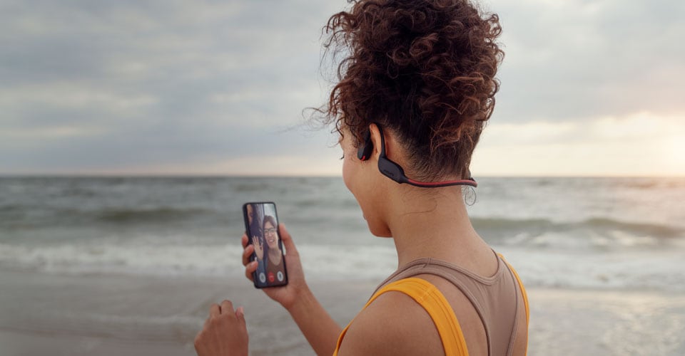 Athletin, die am Strand mit Kopfhörern mit Knochenschall-Übertragung telefoniert