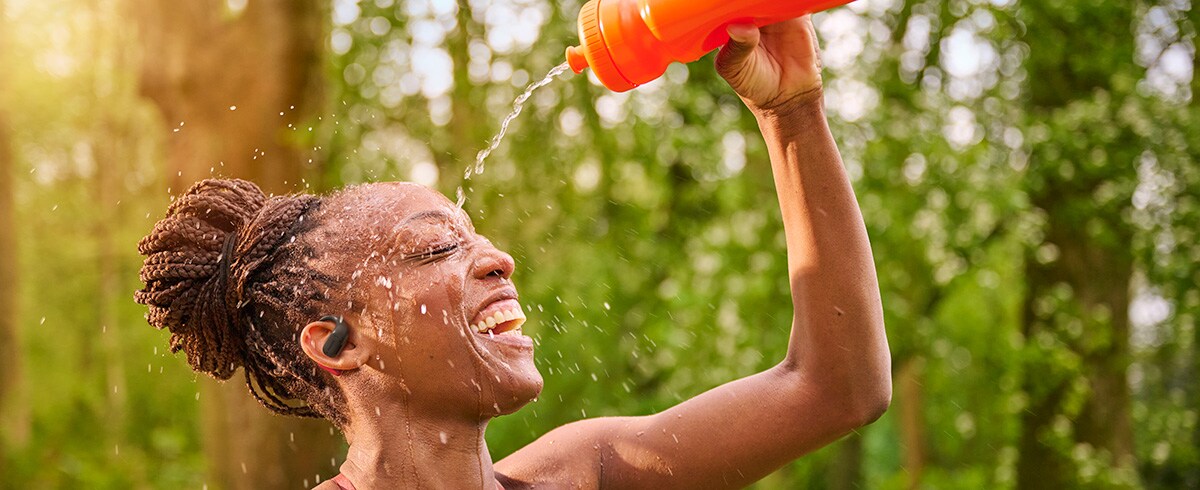 Frau kühlt sich ab, indem sie sich Wasser über den Kopf gießt, während sie Philips Sportkopfhörer im Freien trägt
