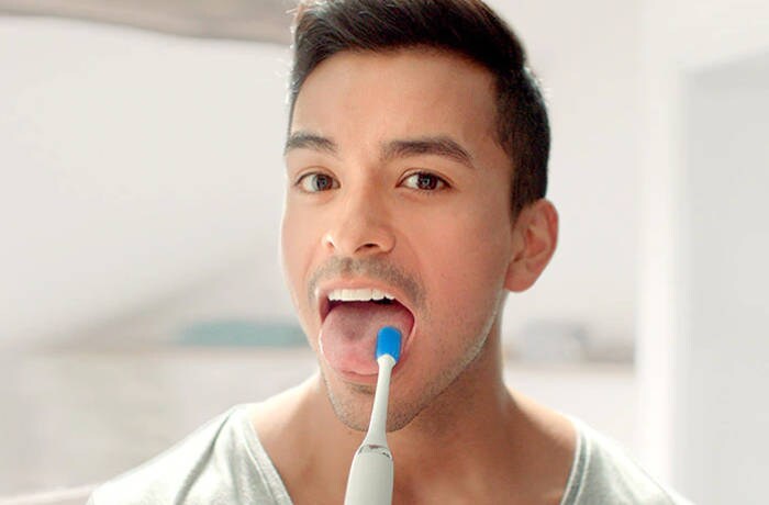Ein Mann schaut in die Kamera und reinigt seinen Zungenbelag mit einer speziellen Philips Zungenbürste.