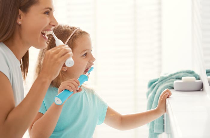 Ein junges Mädchen und ihre Mutter putzen ihre weißen Zähne mit elektrischen Zahnbürsten.