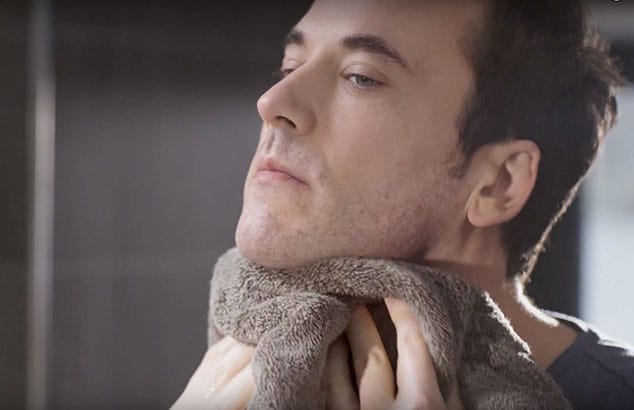 Ein Mann trocknet seinen Hals mit einem Handtuch nach der Rasur ab.