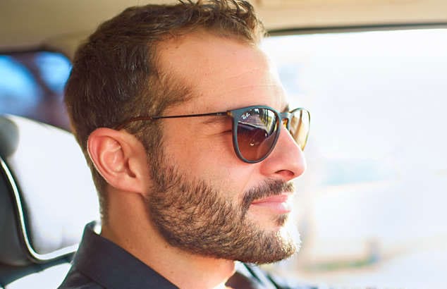 Seitenprofil eines Mannes, der in einem Auto sitzt mit kurzem Vollbart und Sonnenbrille.