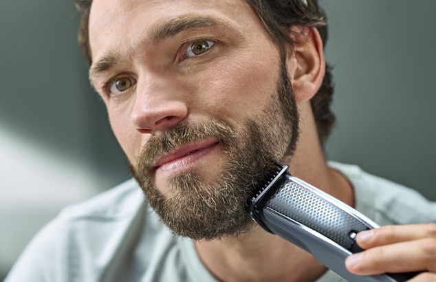 Ein Mann trimmt seinen Bart mit einem elektrischen Barttrimmer von Philips.