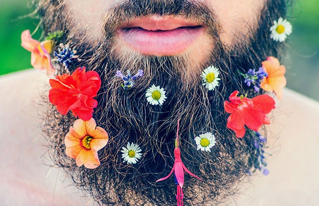 : Untere Gesichtshälfte eines Mannes mit langem Bart, der mit Blumen geschmückt ist.