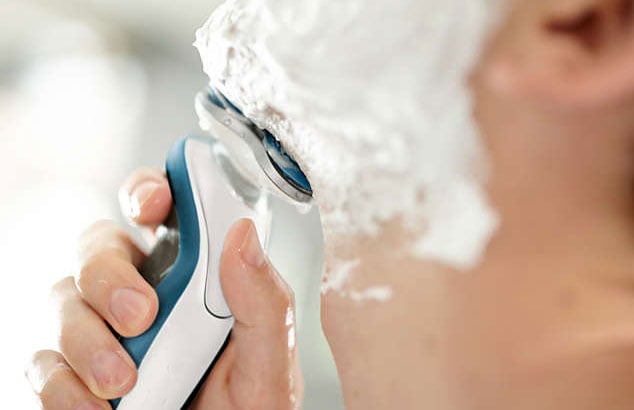 Ein Mann rasiert sich mit einem wasserfesten, elektrischen Rasierer und Rasierschaum.