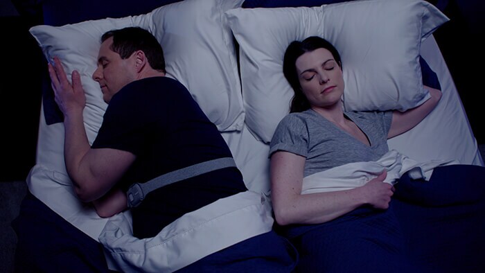 Paar schläft im Bett, eine Person trägt das Snoring Relief Band